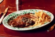 A green and white patterned plate filled with entrecôte à l'anchoïade and a pile of French fries