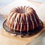 An espresso cake drizzled with glaze on a wire rack that is set on a pice of parchment to catch any glaze drips.