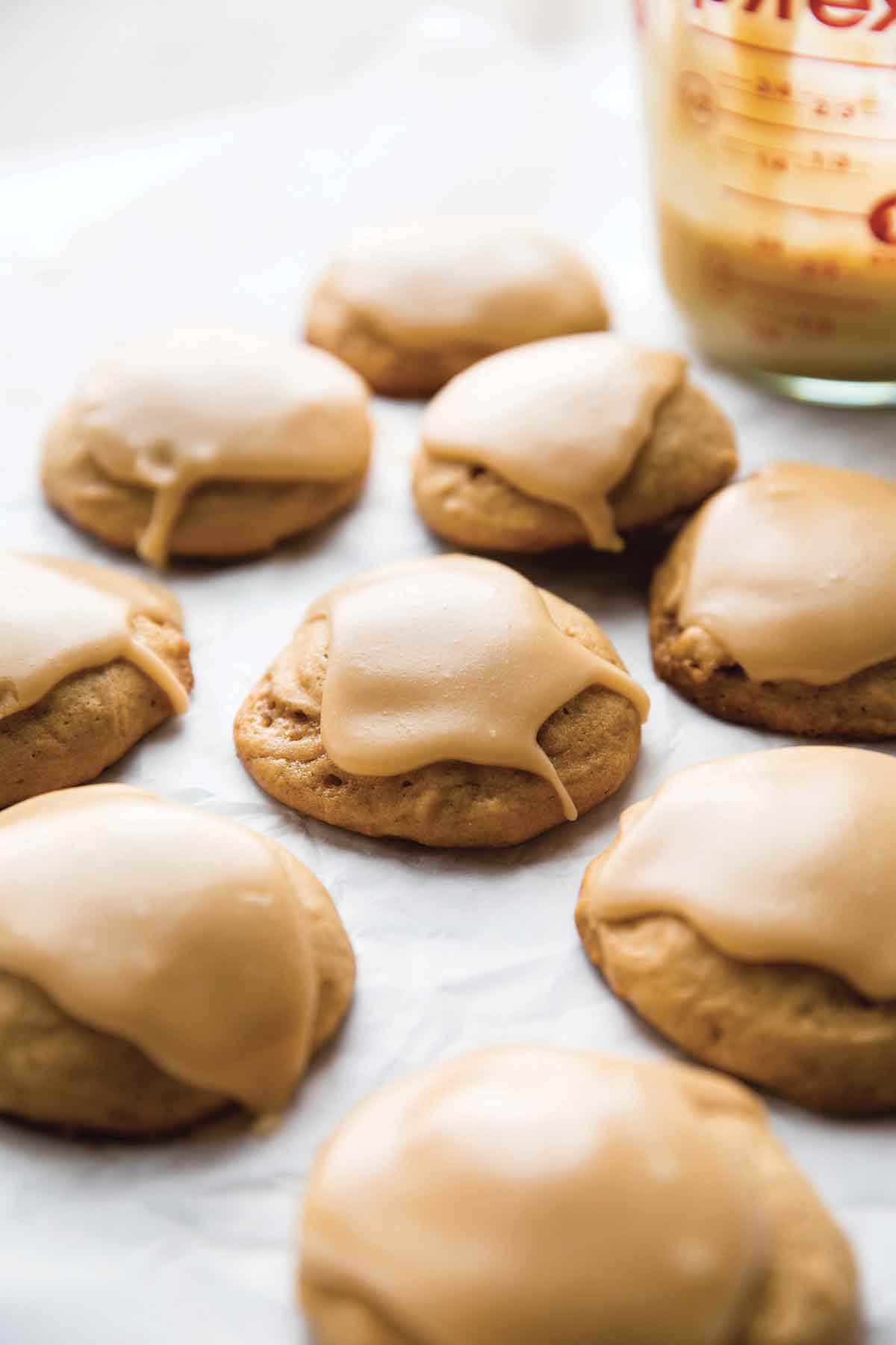 Nine glazed soft maple cookies with a Pyrex container of glaze behind them.