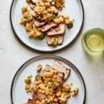 Two white plates topped with sliced grilled pork chops with pineapple and basil and corn and jalapeno.
