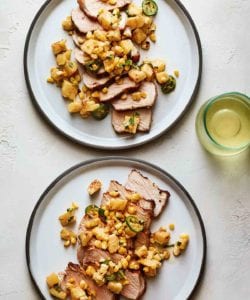 Two white plates topped with sliced grilled pork chops with pineapple and basil and corn and jalapeno.