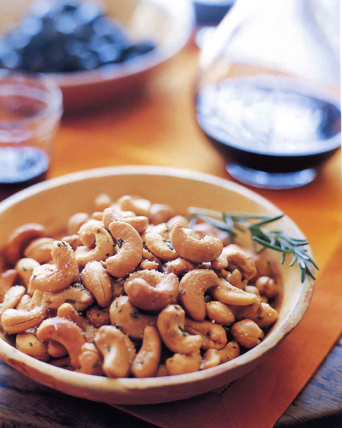 A bowl filled with Ina Garten's rosemary cashews with a sprig of rosemary on the side.