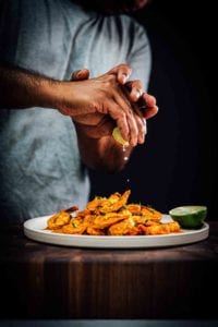 A person squeezing a lime wedge over a plate of masala shrimp.