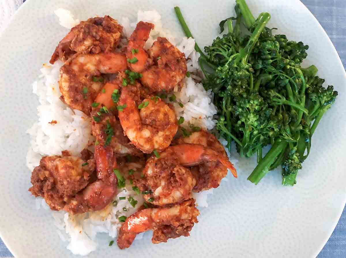 A white plate with masala shrimp, white rice, and steamed broccolini on a blue placemat.