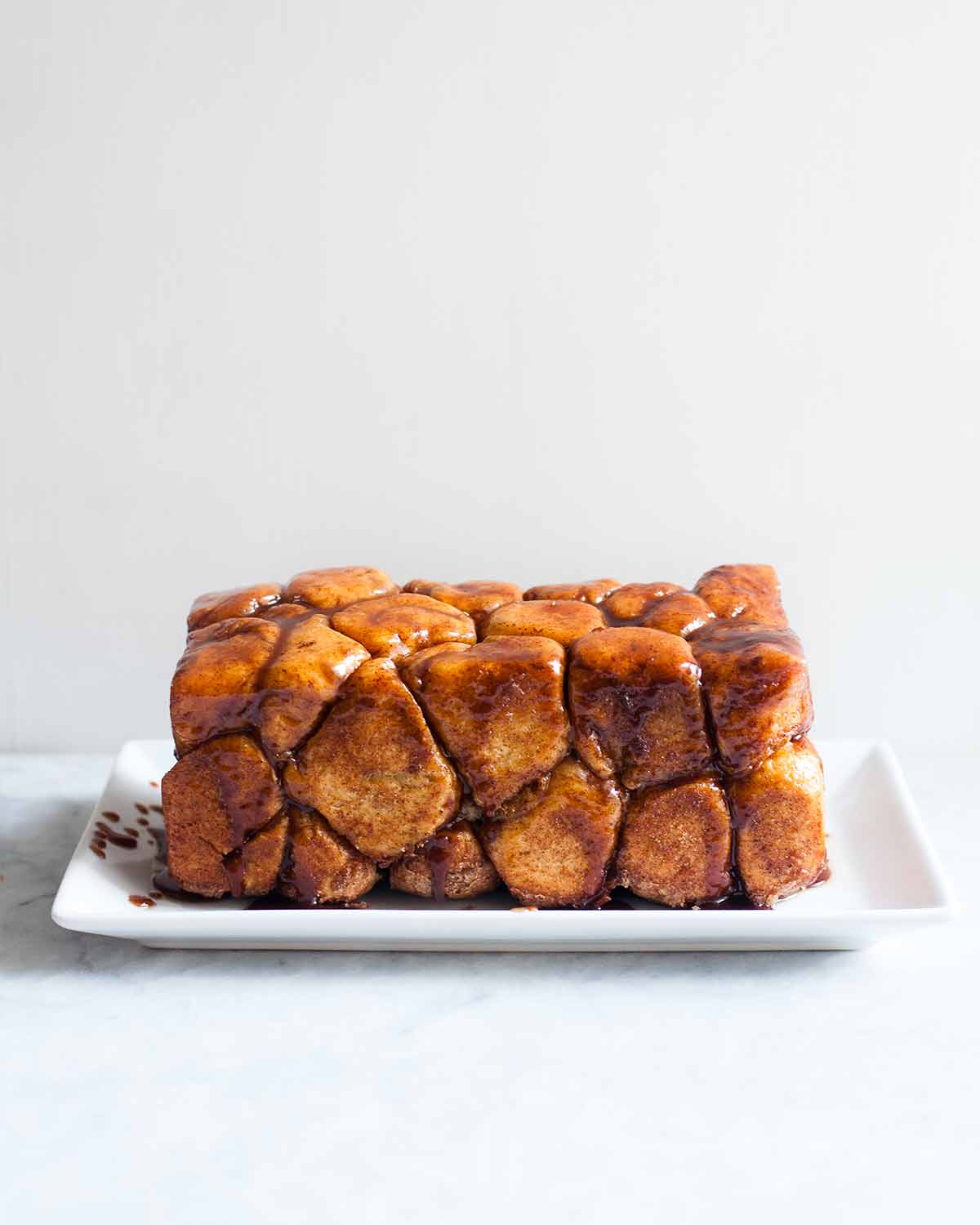 A loaf of monkey bread--balls of caramel-coated bread dough dripping caramel sauce on a rectangle plate