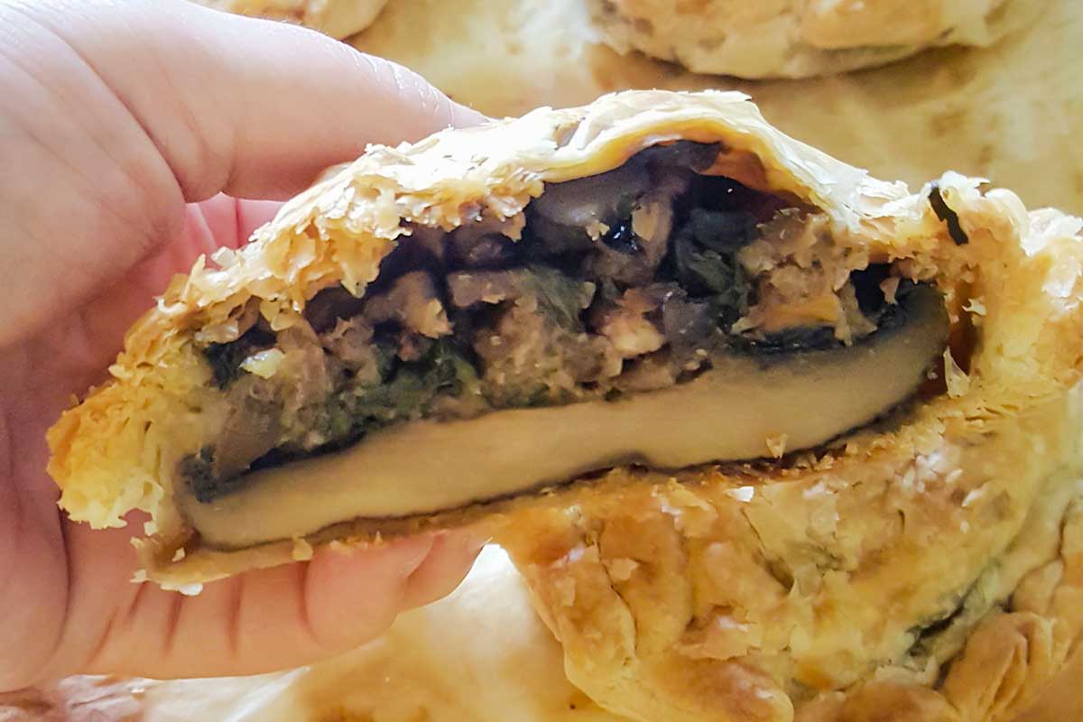 A person holding a halved mushroom wellington with spinach and walnuts.