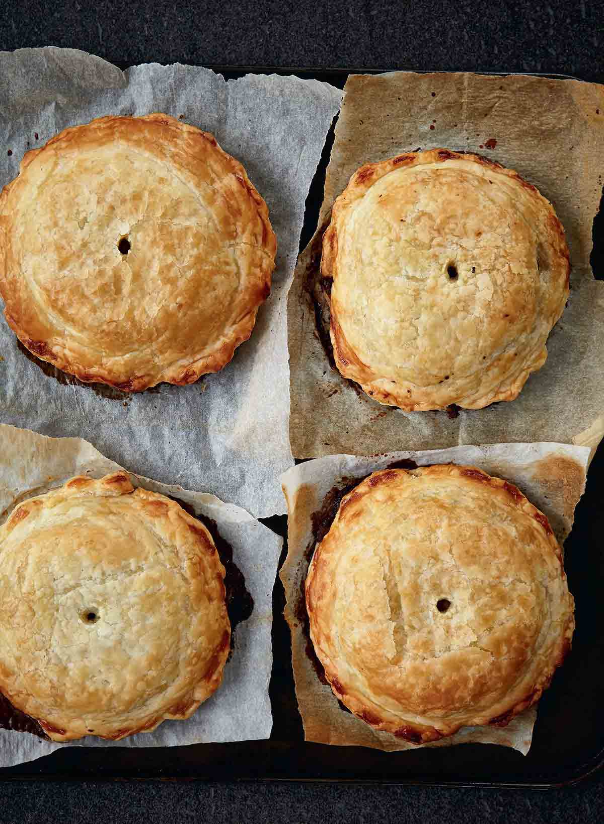 Four individual mushroom wellingtons with spinach and walnuts on a squares of parchment paper.