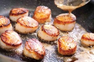 A skillet filled with pan seared scallops cooked in butter.