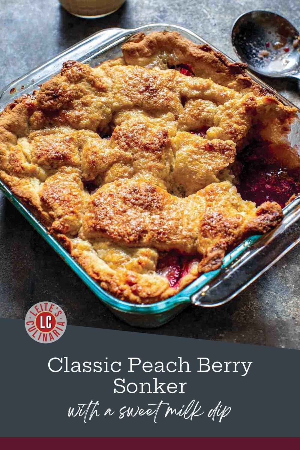 Golden-brown pastry crust covers a bubbling peach-and-berry filling in a glass baking dish beside warm milk dip.