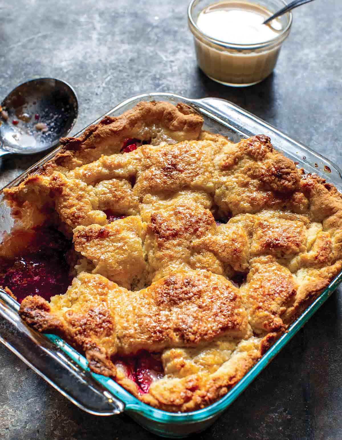 A peach berry sonker in a square baking dish with one serving missing.