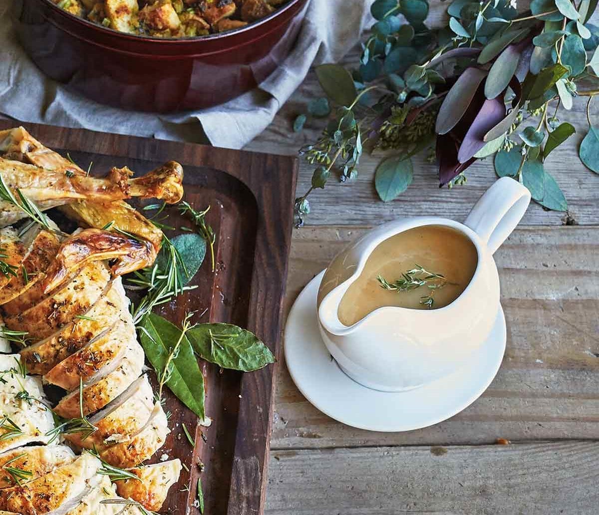 Porcelain Gravy Boat with Saucer on wood table next to sliced turkey.