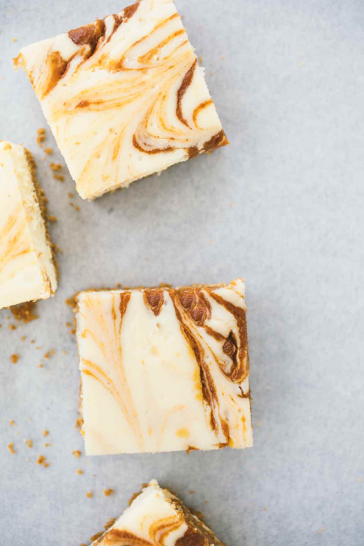 Four pumpkin swirl cheesecake bars on a white surface.