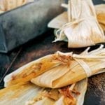 Two wrapped tamales on top of an open corn husk