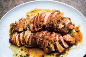 White plate of sliced pork tenderloin with paprika drizzled with a garlic butter sauce