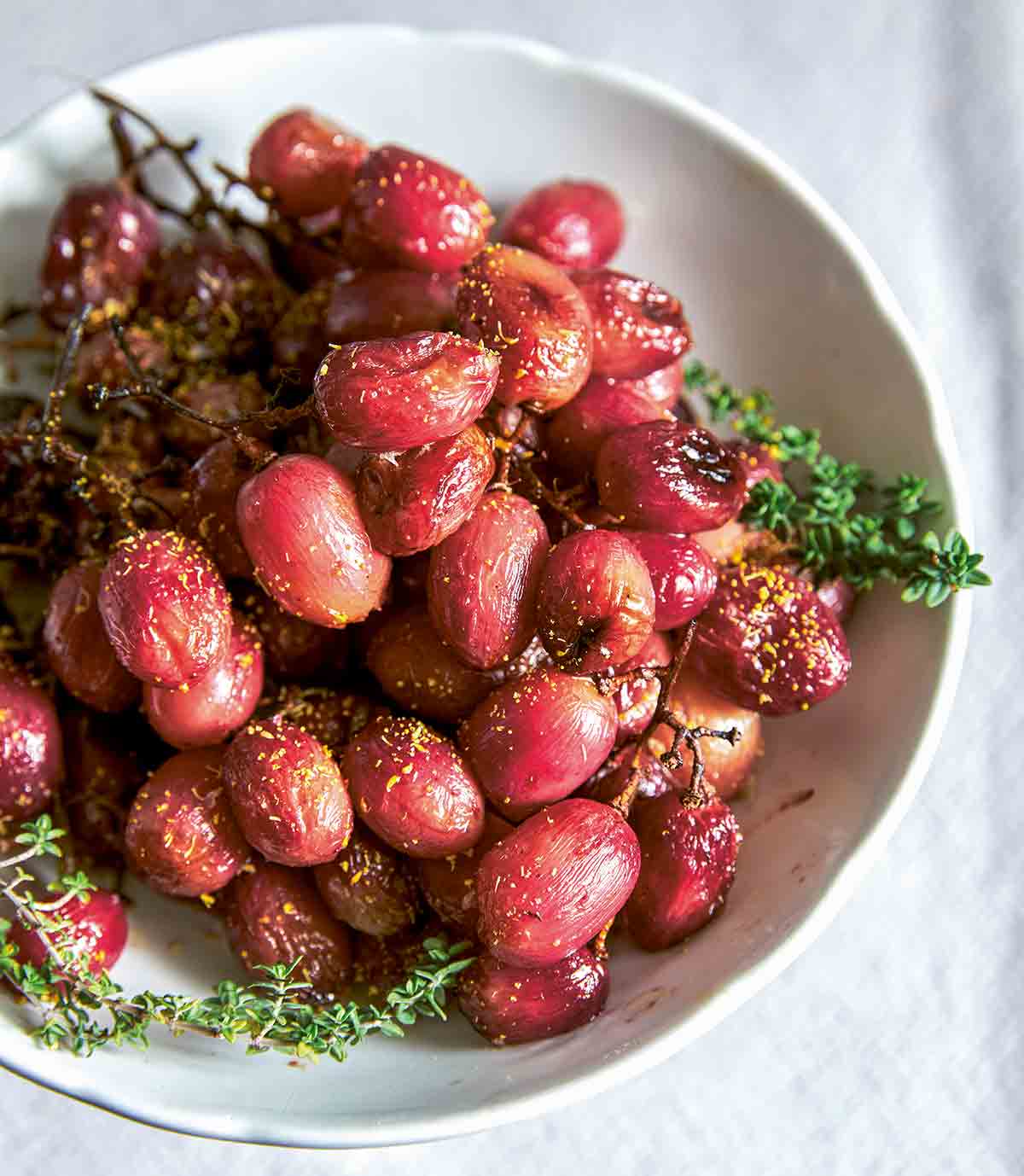 Several bunches of roasted grapes on the vine in a white bowl.