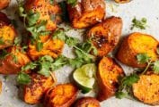Chunks of roasted sweet potatoes with Sriracha and lime wedges and sprigs of cilantro scattered over the top.
