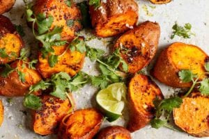 Chunks of roasted sweet potatoes with Sriracha and lime wedges and sprigs of cilantro scattered over the top.