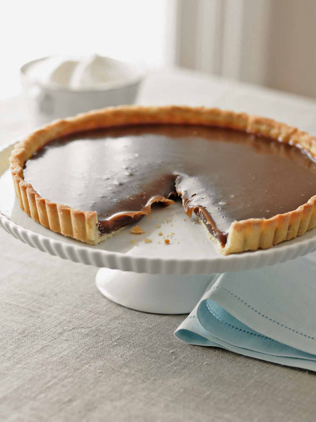 A salted caramel tart on a white cake stand on a table