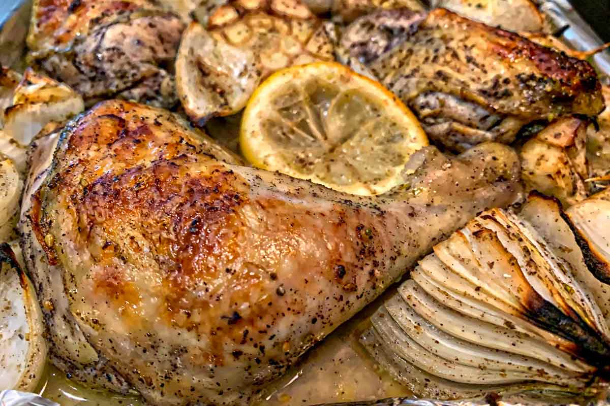 Pieces of sheet pan roast chicken with za'atar with onion wedges, halved garlic heads, and lemon slices.