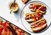 Three sheet pan sausage, peppers, and onions on a white plate with a jar of mustard beside it.