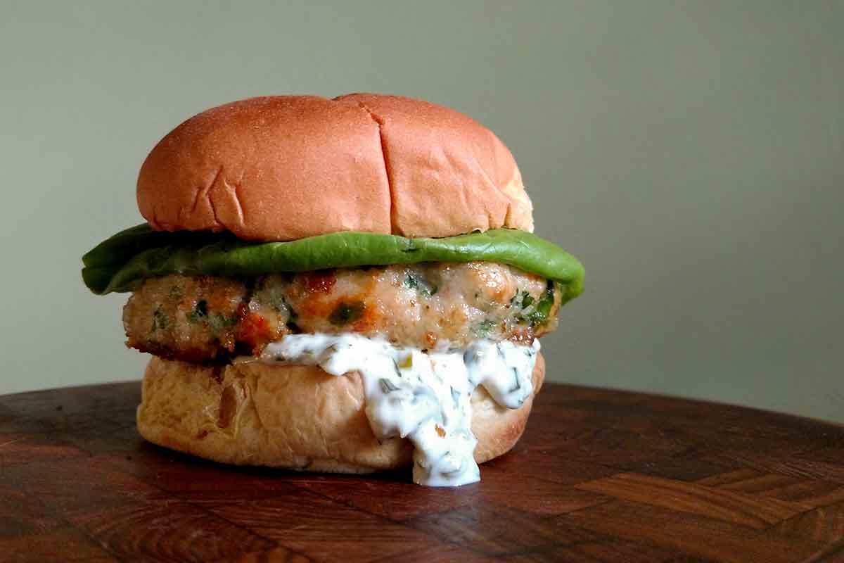 A shrimp burger with tartar sauce, topped with lettuce in a white bun on a wooden table.