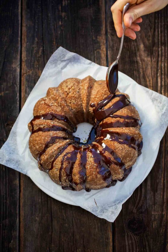 A spiced sweet potato bundt cake on a piece of parchment, being drizzled with chocolate glaze.