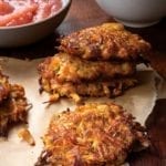 Several sweet potato and apple latkes on a paper towel with a bowl of applesauce in the background.