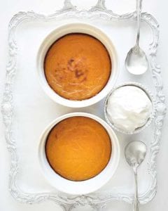 Two sweet potato puddings in white souffle dishes on a silver tray with spoons and a bowl of whipped cream beside them.