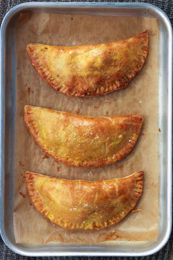 Three leftovers turnovers on a parchment-lined small rimmed baking sheet.