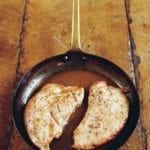 Two turkey cutlets with Marsala sauce in a skillet on a wooden table.
