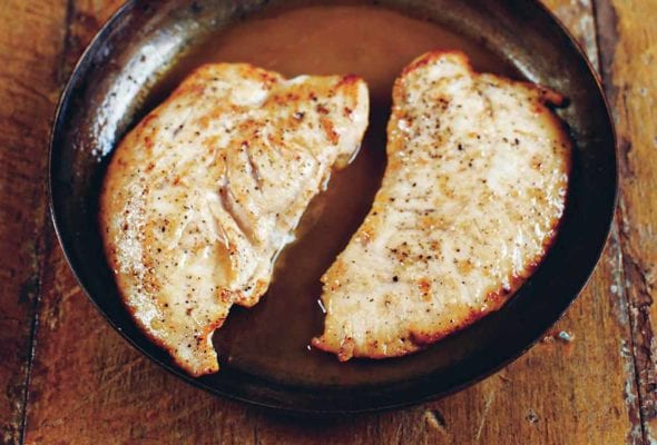 Two turkey cutlets with Marsala sauce in a skillet on a wooden table.