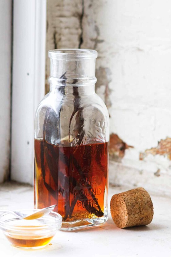 A bottle half-filled with vanilla syrup and a couple vanilla beans inside. A cork rests beside the bottle.