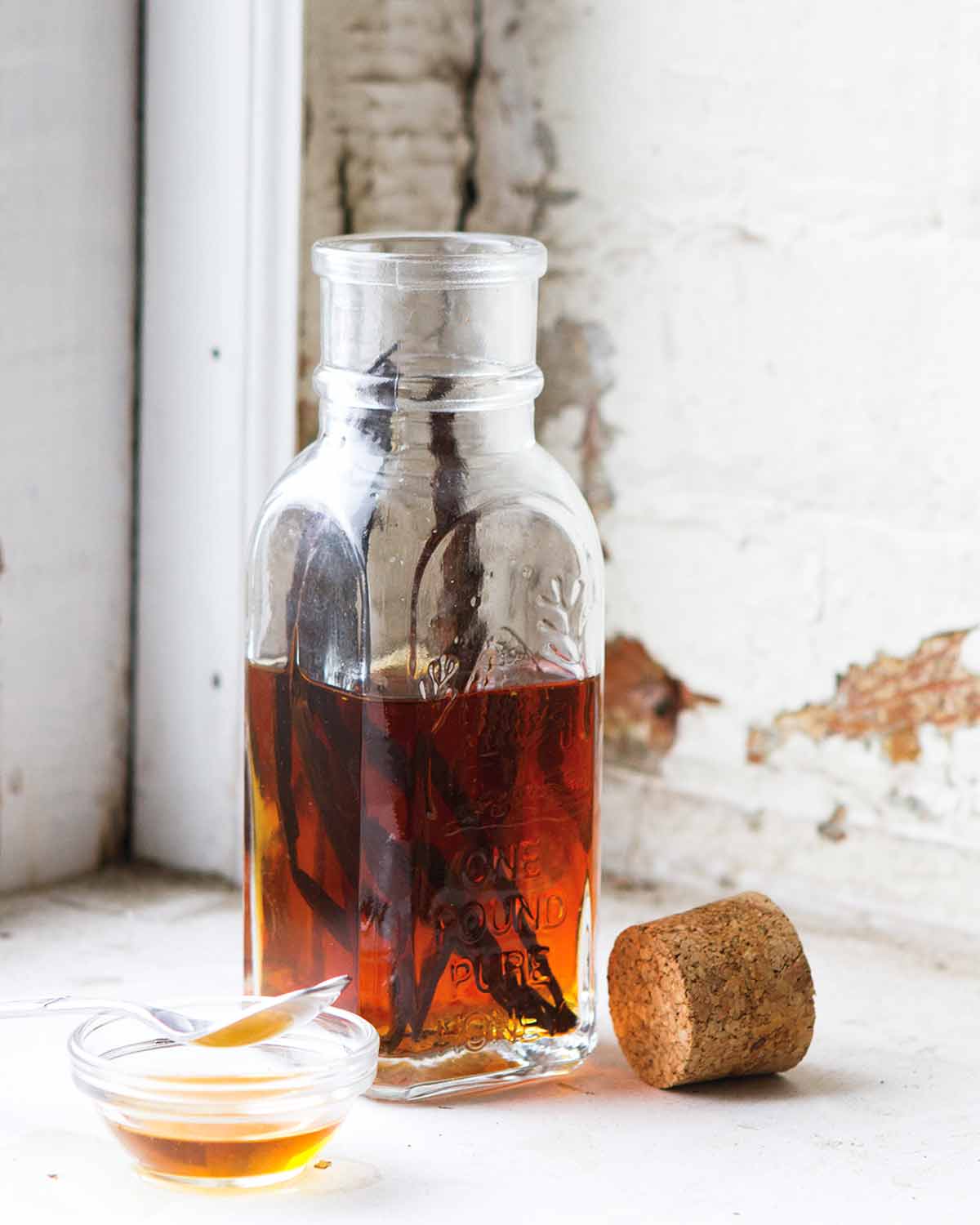 A bottle half-filled with vanilla syrup and a couple vanilla beans inside. A cork rests beside the bottle.