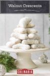 Walnut crescents stacked on a white stand with Christmas decorations and greenery around them.