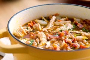A yellow Dutch oven filled with white bean and chicken chili, topped with pieces of bacon.