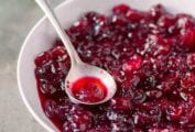 A white bowl filled with whole berry cranberry sauce with a silver spoon resting in it.