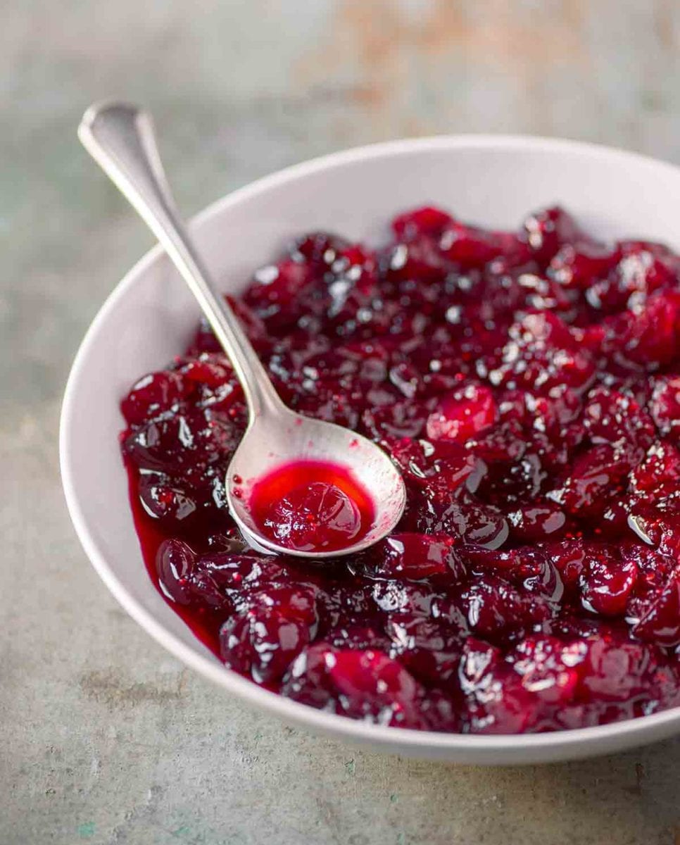 A white bowl filled with whole berry cranberry sauce with a silver spoon resting in it.