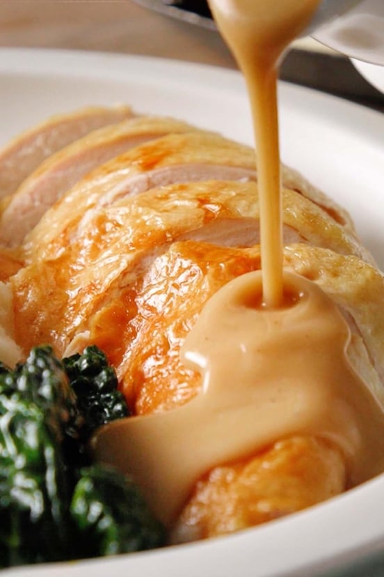 Golden, rich gravy being poured over a plate of sliced turkey breast.