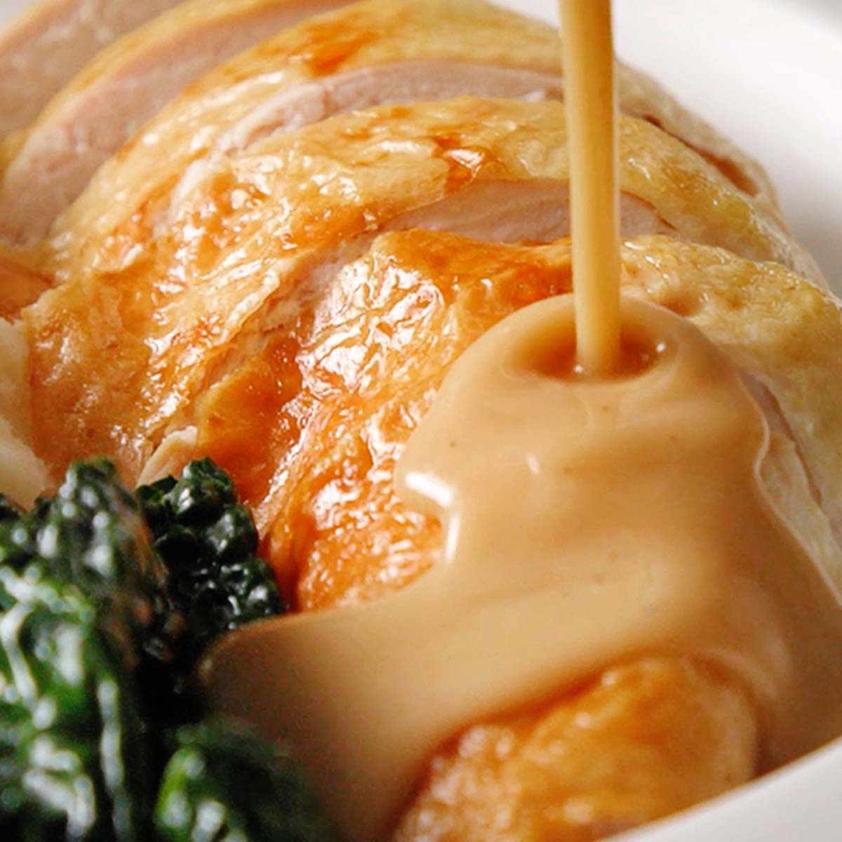 A no-fail pan gravy being poured over sliced turkey breast on a plate with greens.