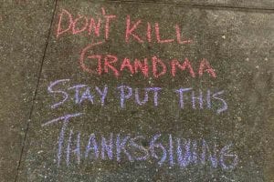 A chalk sidewalk writing that says 'don't kill grandma stay put this Thanksgiving' to illustrate how to have a satisfying Thanksgiving on Zoom (Honest).