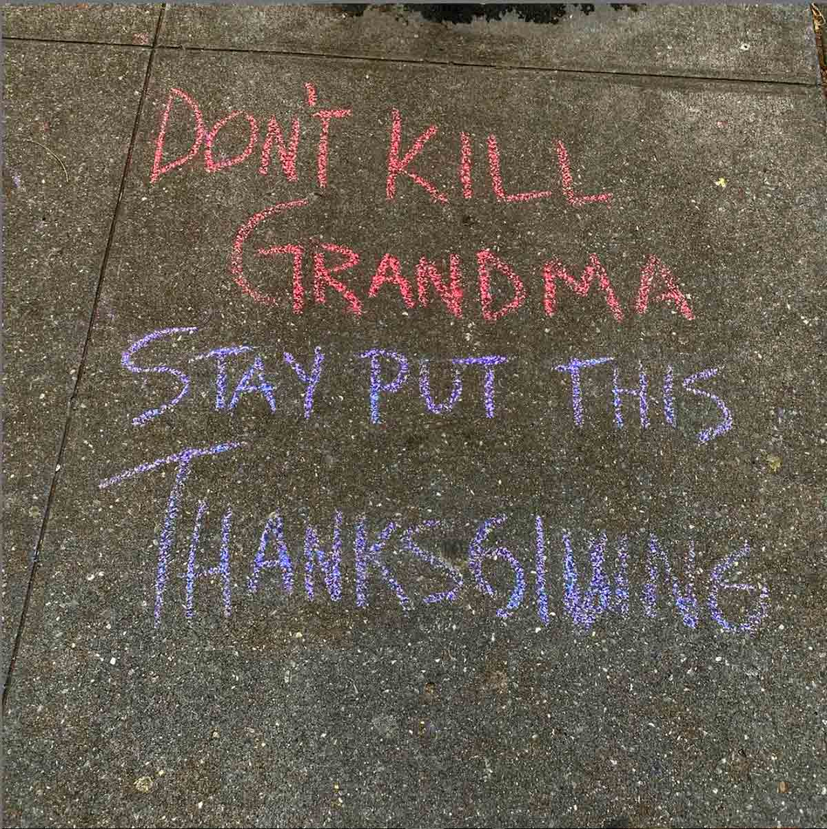 A chalk sidewalk writing that says 'don't kill grandma stay put this Thanksgiving' to illustrate how to have a satisfying Thanksgiving on Zoom (Honest).