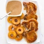 Four French-style pork chops with apples and Calvados sauce on a white platter.