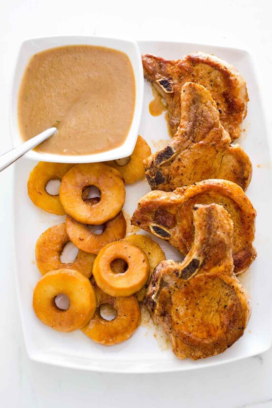 Four French-style pork chops with apples and Calvados sauce on a white platter.