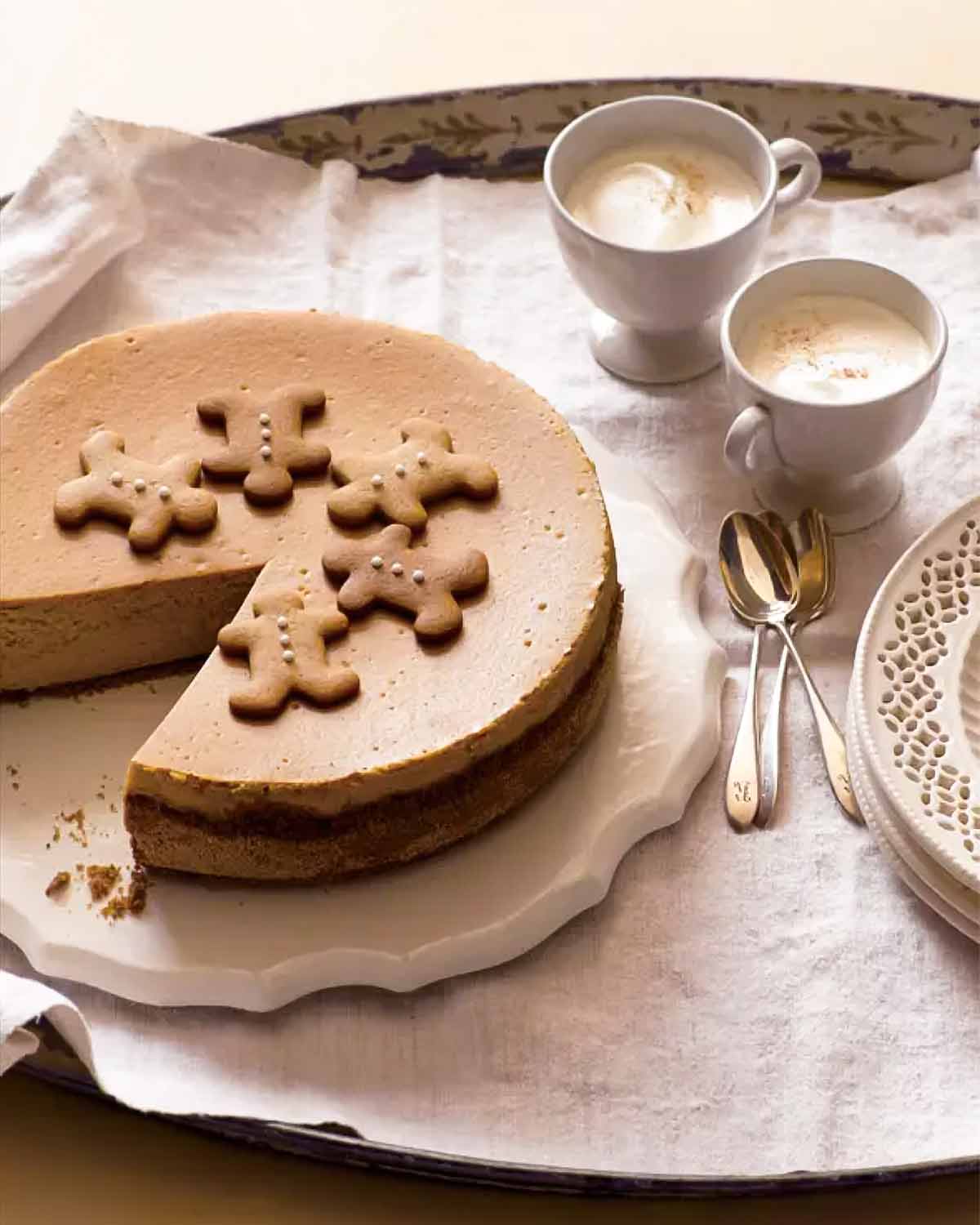 A whole gingerbread cheesecake on a white platter with a slice missing from it.