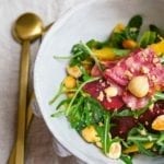 A white bowl filled with raw beet and hazelnut salad with a gold spoon beside the bowl.