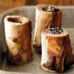 Three pieces of roasted bone marrow sprinkled with salt in a metal roasting pan.