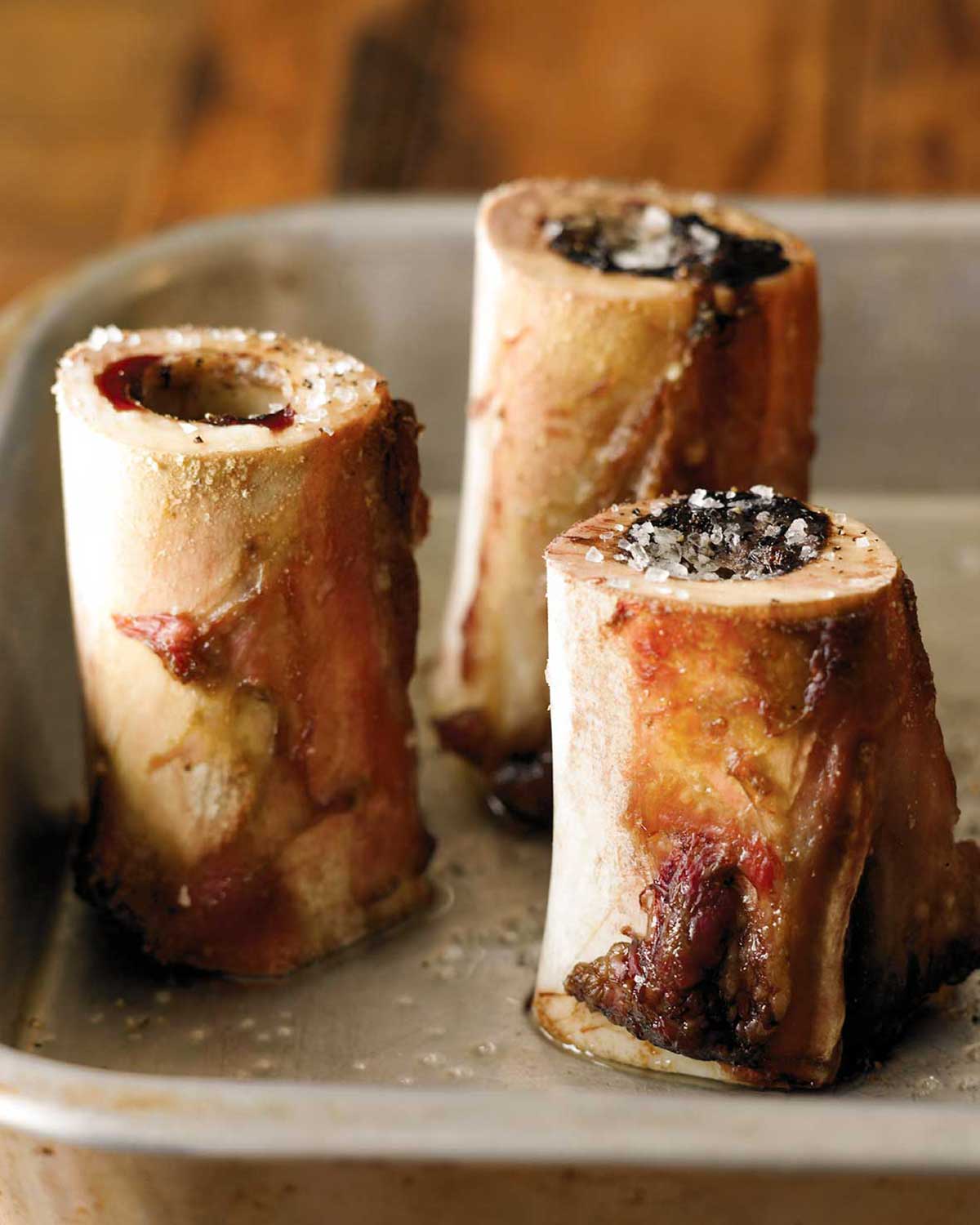 Three pieces of roasted bone marrow sprinkled with salt in a metal skillet.