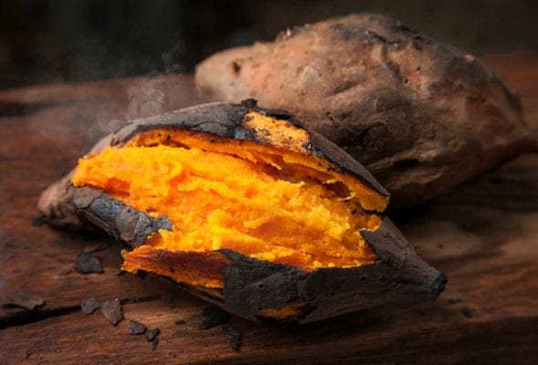 Two roasted sweet potatoes on a wooden table.