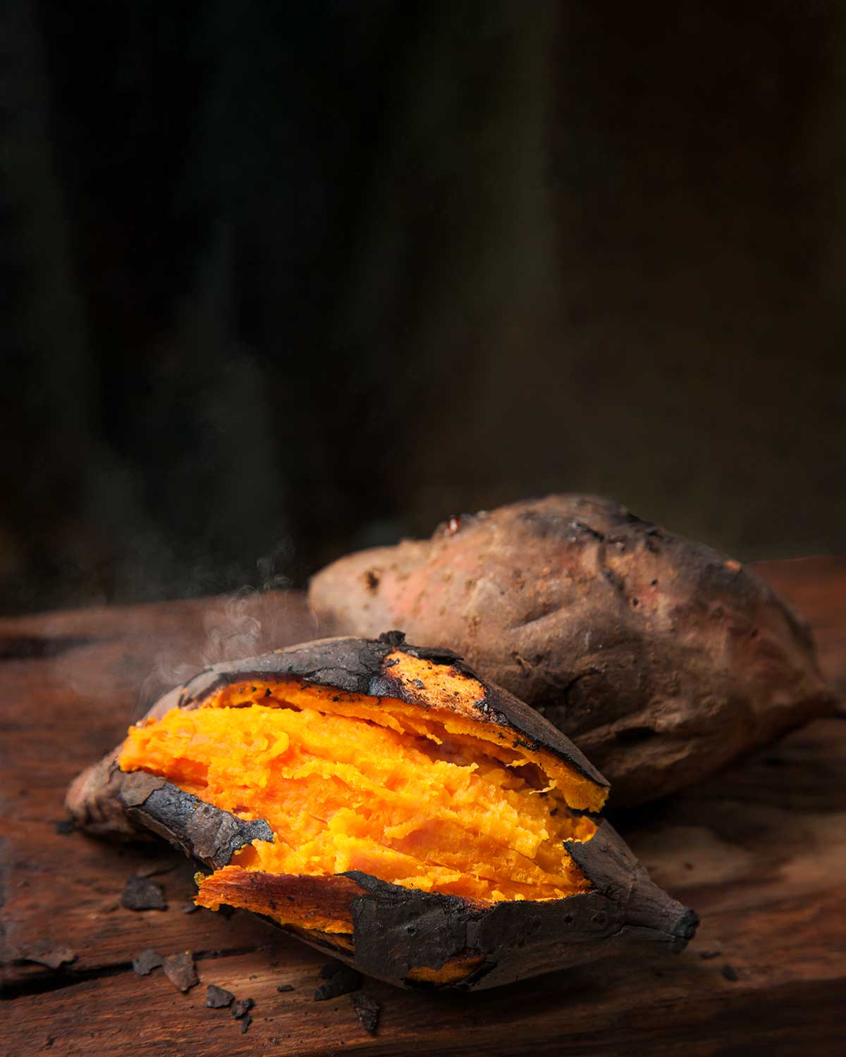 Two roasted sweet potatoes on a wooden table.