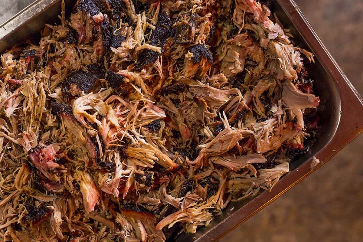 Shredded slow cooker pulled pork in a metal dish.